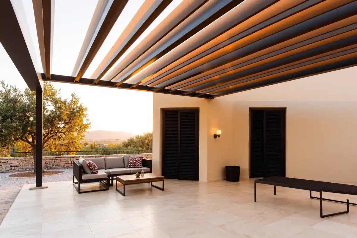 Bronze aluminium louvred pergola casting striped shadows over a Mediterranean terrace lounge